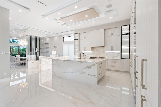 kitchen featuring sink, light stone counters, an inviting chandelier, a large island, and decorative backsplash