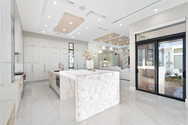 kitchen with white cabinetry, oven, sink, and a large island with sink