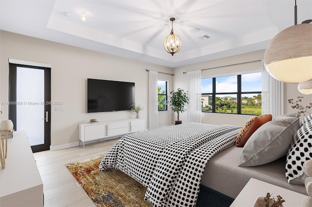 bedroom featuring a tray ceiling, an inviting chandelier, and light hardwood / wood-style flooring