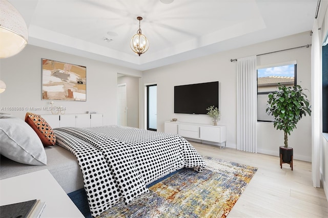 bedroom featuring light hardwood / wood-style flooring, a chandelier, and a raised ceiling