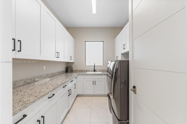 kitchen featuring white cabinetry, sink, light stone counters, and washing machine and clothes dryer