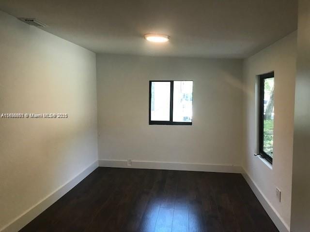 spare room featuring visible vents, baseboards, and dark wood-type flooring