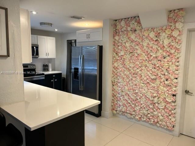 kitchen featuring kitchen peninsula, white cabinets, light tile patterned floors, and appliances with stainless steel finishes