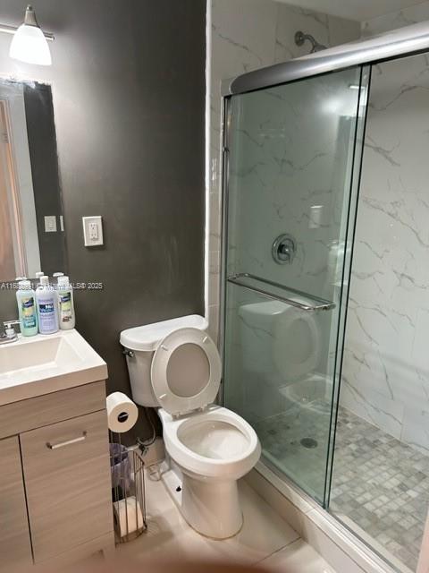 bathroom with tile patterned floors, vanity, toilet, and a shower with door