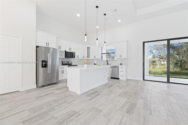 kitchen featuring a towering ceiling, a kitchen island, appliances with stainless steel finishes, pendant lighting, and white cabinets