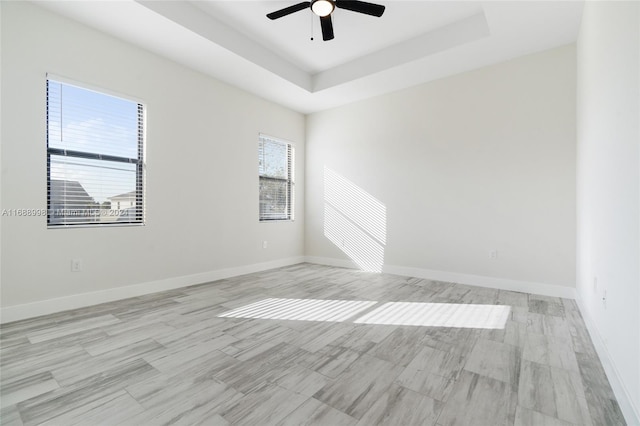 unfurnished room with ceiling fan, a tray ceiling, a healthy amount of sunlight, and light hardwood / wood-style flooring