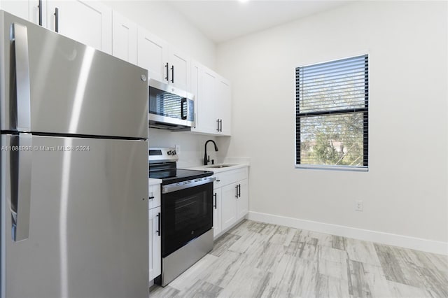 kitchen featuring stainless steel appliances, white cabinets, sink, and light wood-type flooring