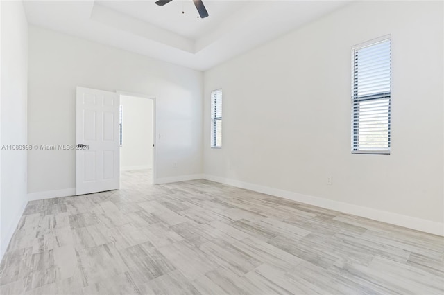 spare room with ceiling fan, light wood-type flooring, and a tray ceiling