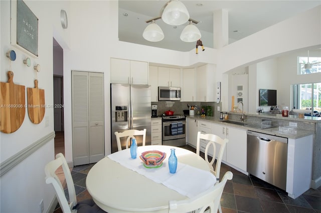 kitchen featuring white cabinets, a towering ceiling, stainless steel appliances, and decorative backsplash