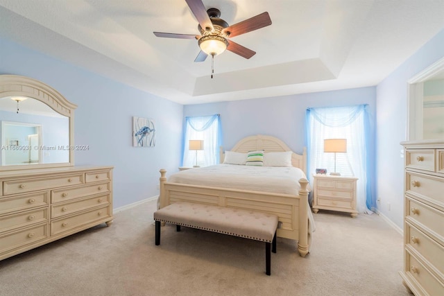 bedroom featuring ceiling fan, multiple windows, a tray ceiling, and light colored carpet