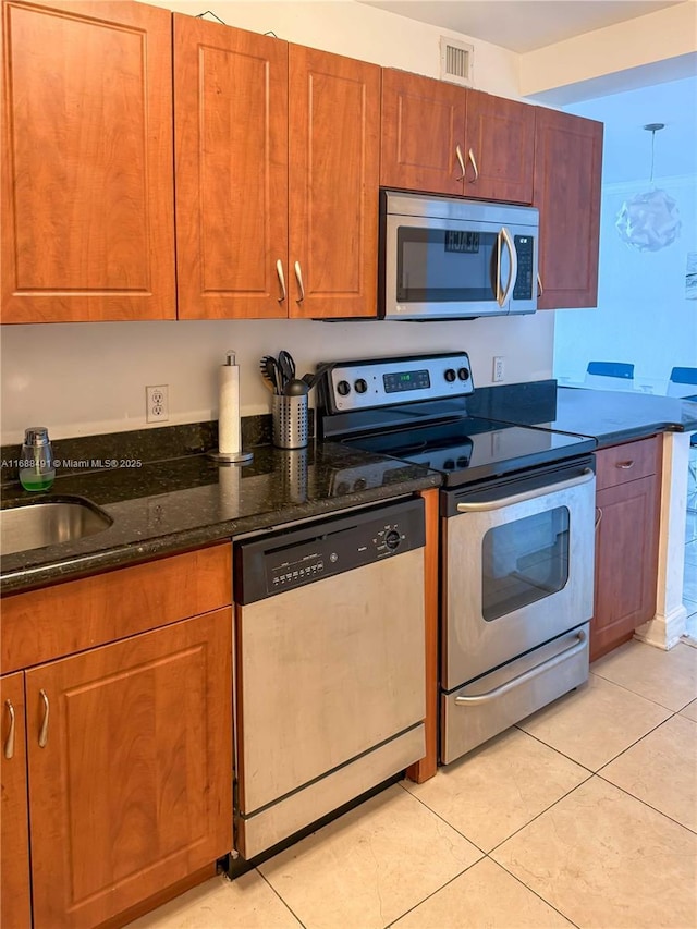 kitchen with sink, stainless steel appliances, dark stone counters, and light tile patterned flooring