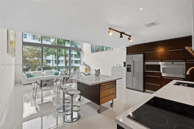 kitchen featuring stainless steel appliances, dark brown cabinetry, light tile patterned floors, sink, and a center island