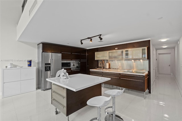 kitchen featuring stainless steel appliances, light tile patterned flooring, sink, a breakfast bar area, and a center island