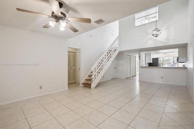 unfurnished living room featuring visible vents, ceiling fan with notable chandelier, a textured ceiling, light tile patterned floors, and stairs