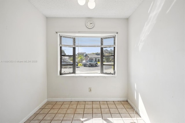 empty room with light tile patterned floors, baseboards, and a textured ceiling