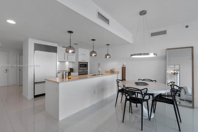 kitchen with decorative light fixtures, white cabinetry, sink, built in appliances, and kitchen peninsula