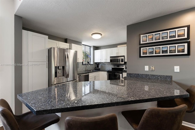 kitchen with appliances with stainless steel finishes, a kitchen bar, sink, white cabinets, and kitchen peninsula