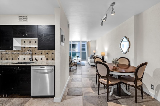 kitchen featuring sink, track lighting, light stone countertops, stainless steel dishwasher, and decorative backsplash