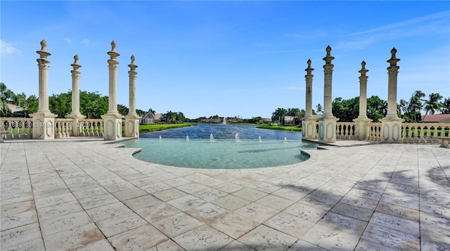 view of swimming pool with pool water feature, a water view, and a patio