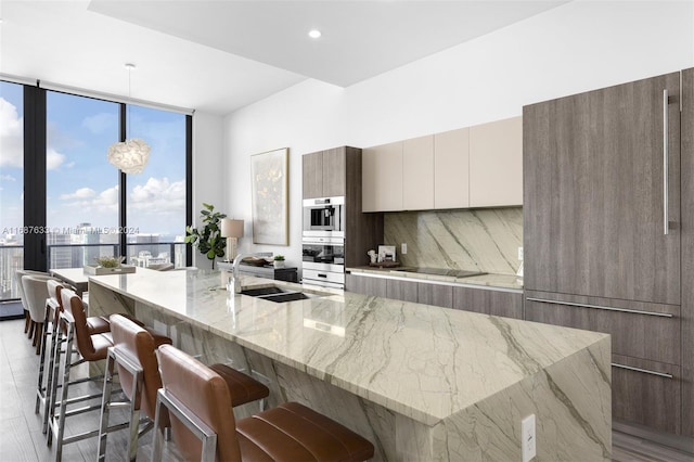 kitchen with light stone countertops, sink, pendant lighting, decorative backsplash, and light wood-type flooring