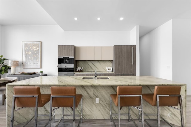 kitchen featuring a breakfast bar, a center island with sink, sink, dark hardwood / wood-style floors, and light stone countertops