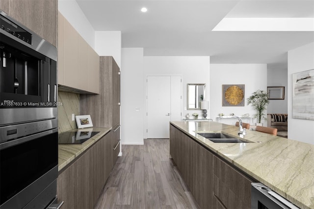 kitchen with black electric stovetop, sink, wine cooler, light wood-type flooring, and light stone counters