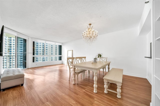 dining area featuring a textured ceiling, light wood-type flooring, an inviting chandelier, and expansive windows