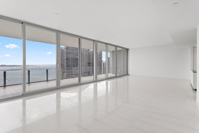 empty room with light tile patterned flooring, a water view, and floor to ceiling windows