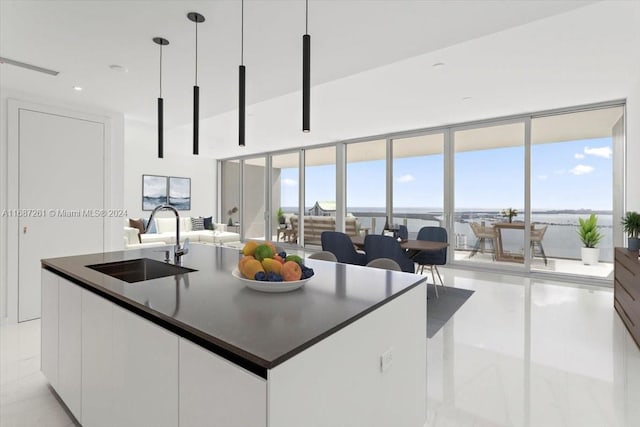 kitchen with decorative light fixtures, white cabinetry, sink, and an island with sink