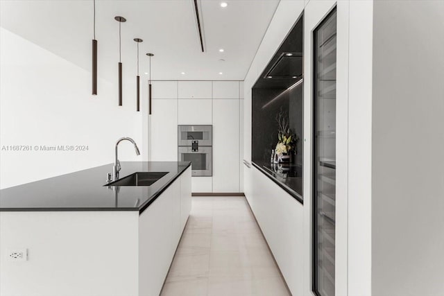 kitchen with pendant lighting, sink, an island with sink, white cabinets, and double oven