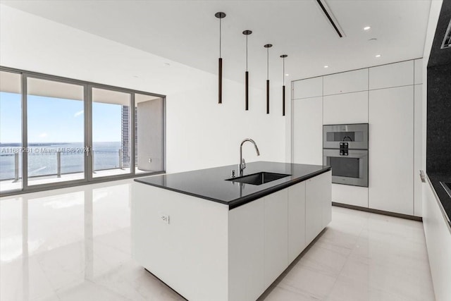 kitchen featuring white cabinetry, sink, a water view, decorative light fixtures, and a kitchen island with sink