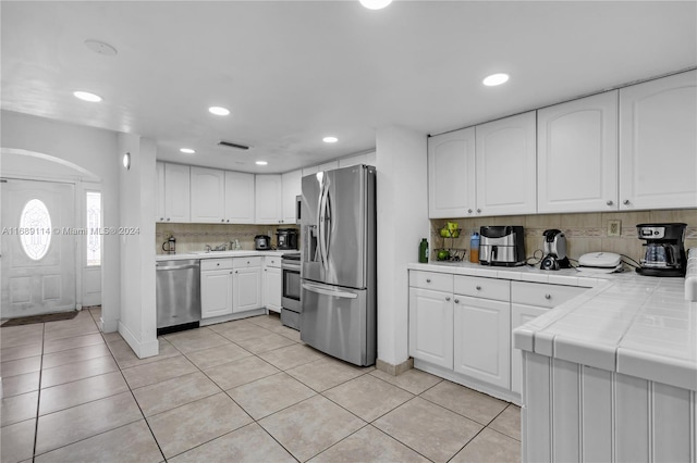 kitchen with stainless steel appliances, tile countertops, tasteful backsplash, light tile patterned floors, and white cabinets