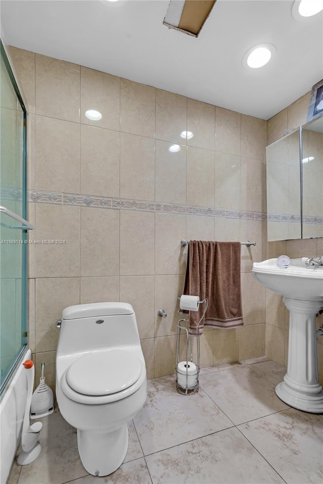 bathroom with tile patterned floors, combined bath / shower with glass door, tile walls, and toilet