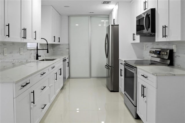 kitchen featuring light stone counters, white cabinets, sink, light tile patterned floors, and appliances with stainless steel finishes