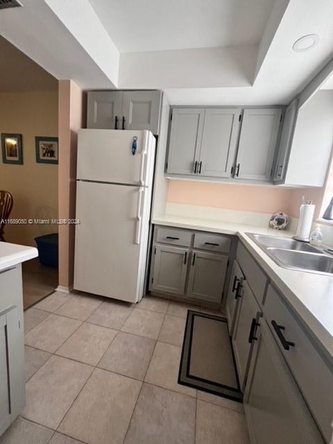 kitchen with light tile patterned floors, gray cabinets, white fridge, and sink