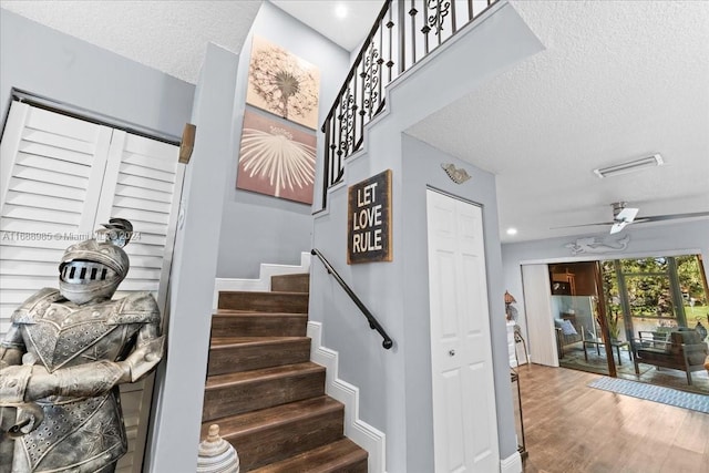 staircase featuring hardwood / wood-style flooring, ceiling fan, and a textured ceiling