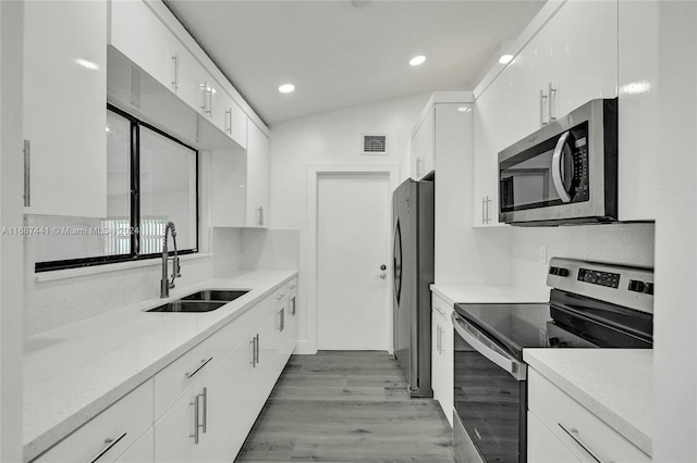 kitchen featuring white cabinets, appliances with stainless steel finishes, lofted ceiling, and light hardwood / wood-style floors