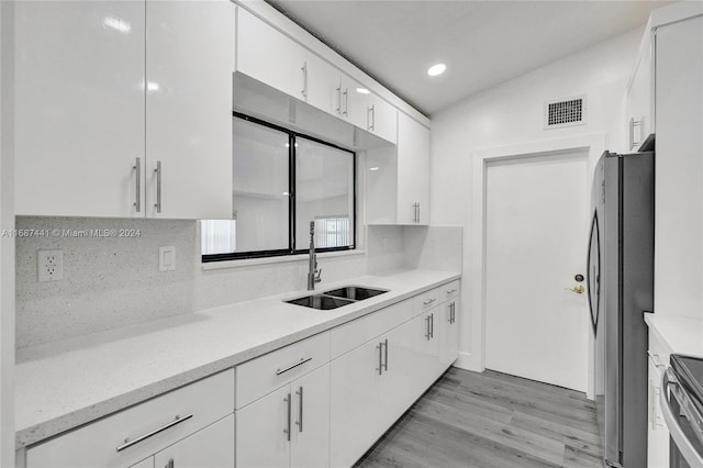 kitchen featuring stainless steel appliances, white cabinetry, sink, light hardwood / wood-style floors, and lofted ceiling