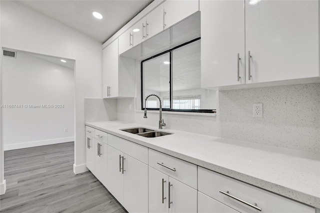 kitchen with white cabinetry, sink, light hardwood / wood-style flooring, and tasteful backsplash