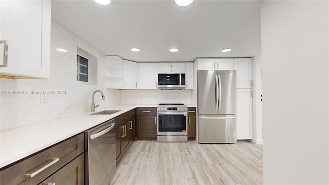 kitchen featuring white cabinetry, sink, appliances with stainless steel finishes, light hardwood / wood-style flooring, and decorative backsplash