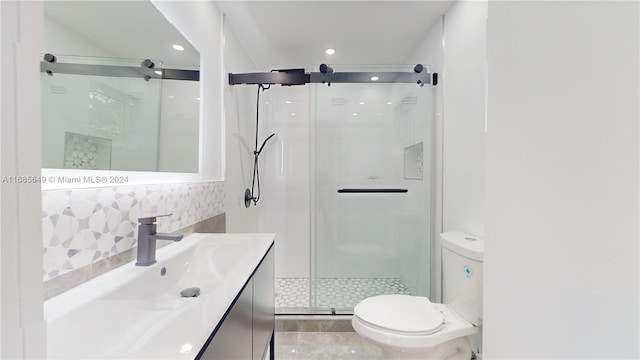 bathroom with toilet, vanity, decorative backsplash, and a shower with door