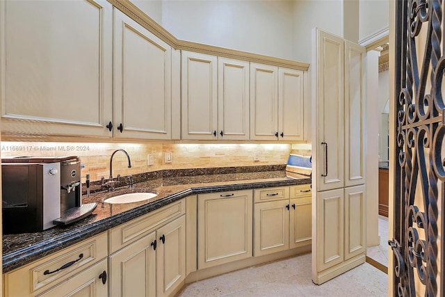 kitchen featuring dark stone countertops, decorative backsplash, sink, and cream cabinetry