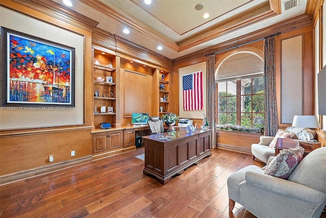 office area with built in desk, built in shelves, ornamental molding, a tray ceiling, and hardwood / wood-style floors