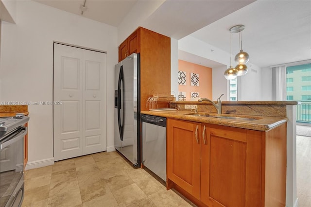 kitchen with stainless steel appliances, light stone counters, kitchen peninsula, sink, and pendant lighting