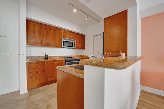 kitchen with stainless steel appliances, track lighting, light stone countertops, sink, and kitchen peninsula