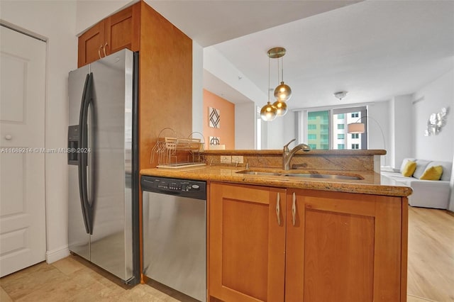 kitchen with light stone counters, appliances with stainless steel finishes, hanging light fixtures, sink, and light hardwood / wood-style flooring