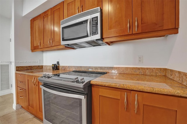 kitchen featuring appliances with stainless steel finishes, light tile patterned floors, and light stone countertops