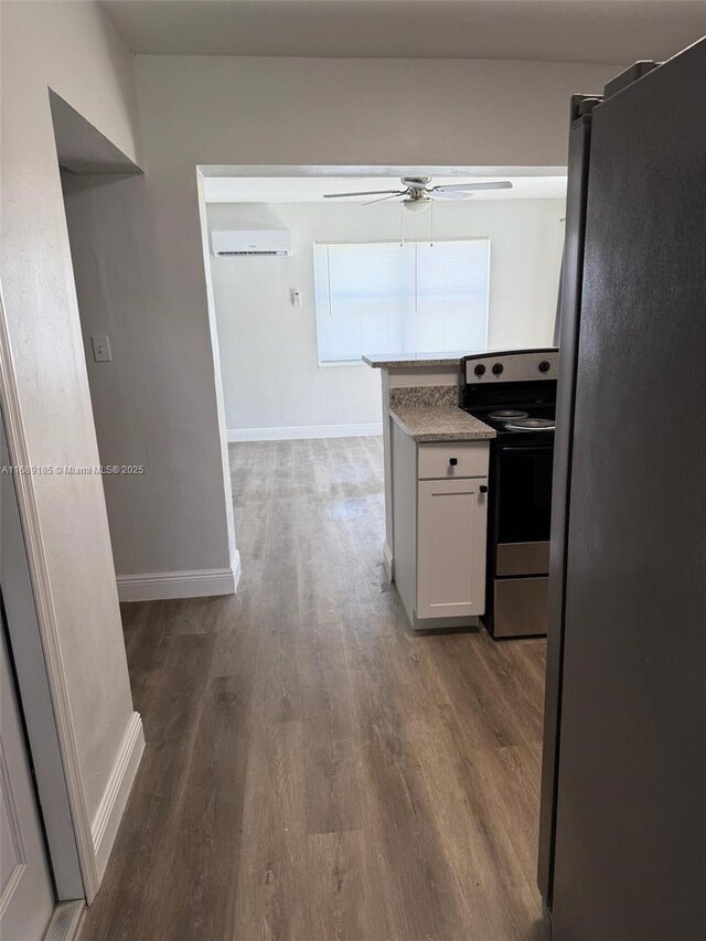 kitchen with ceiling fan, dark wood-type flooring, stainless steel appliances, a wall mounted AC, and white cabinets