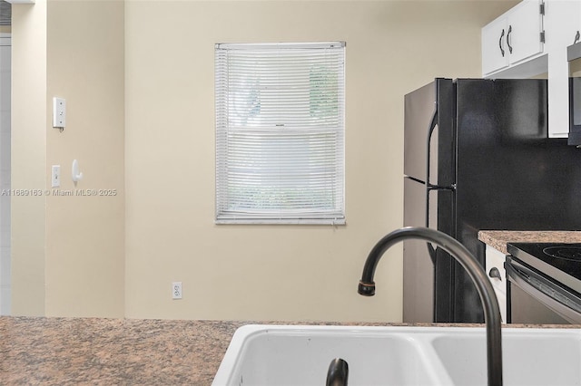 kitchen with white cabinetry, sink, and black refrigerator