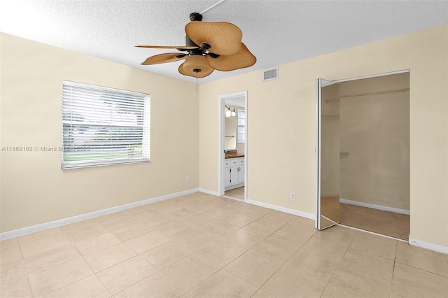 unfurnished bedroom with light tile patterned floors, ceiling fan, connected bathroom, a textured ceiling, and a closet